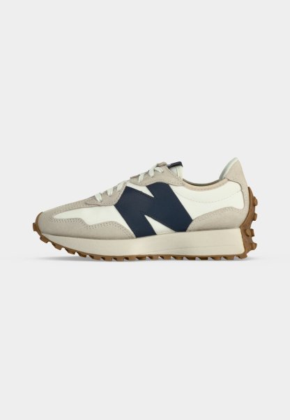 Zapatilla beige y blanca con logo lateral "N" en azul marino, cordones blancos y suela de goma marrón texturizada, mostrada de perfil sobre fondo claro.