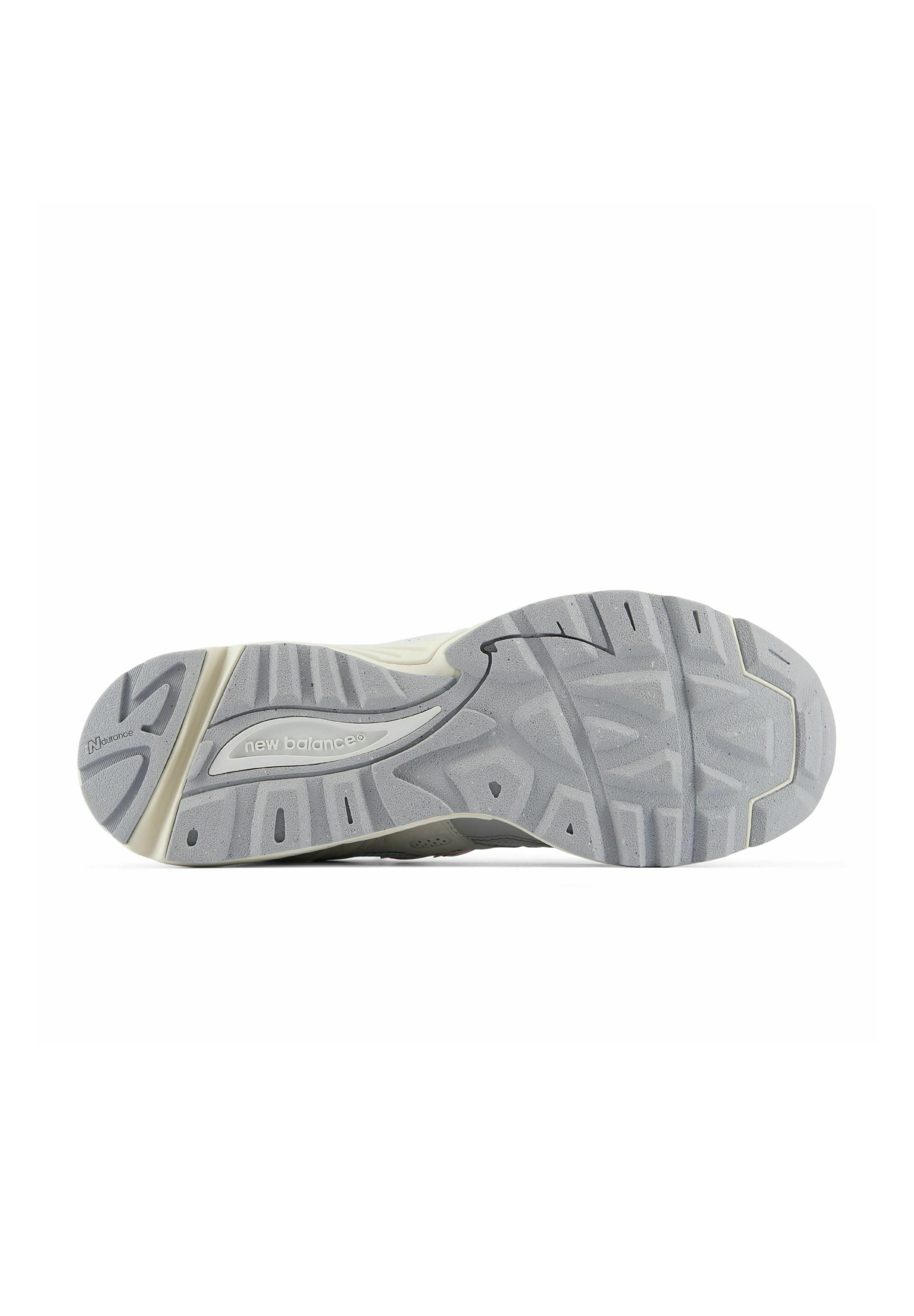 Suela de una zapatilla New Balance que muestra una banda de rodadura gris y beige con agarre estampado y marca New Balance.