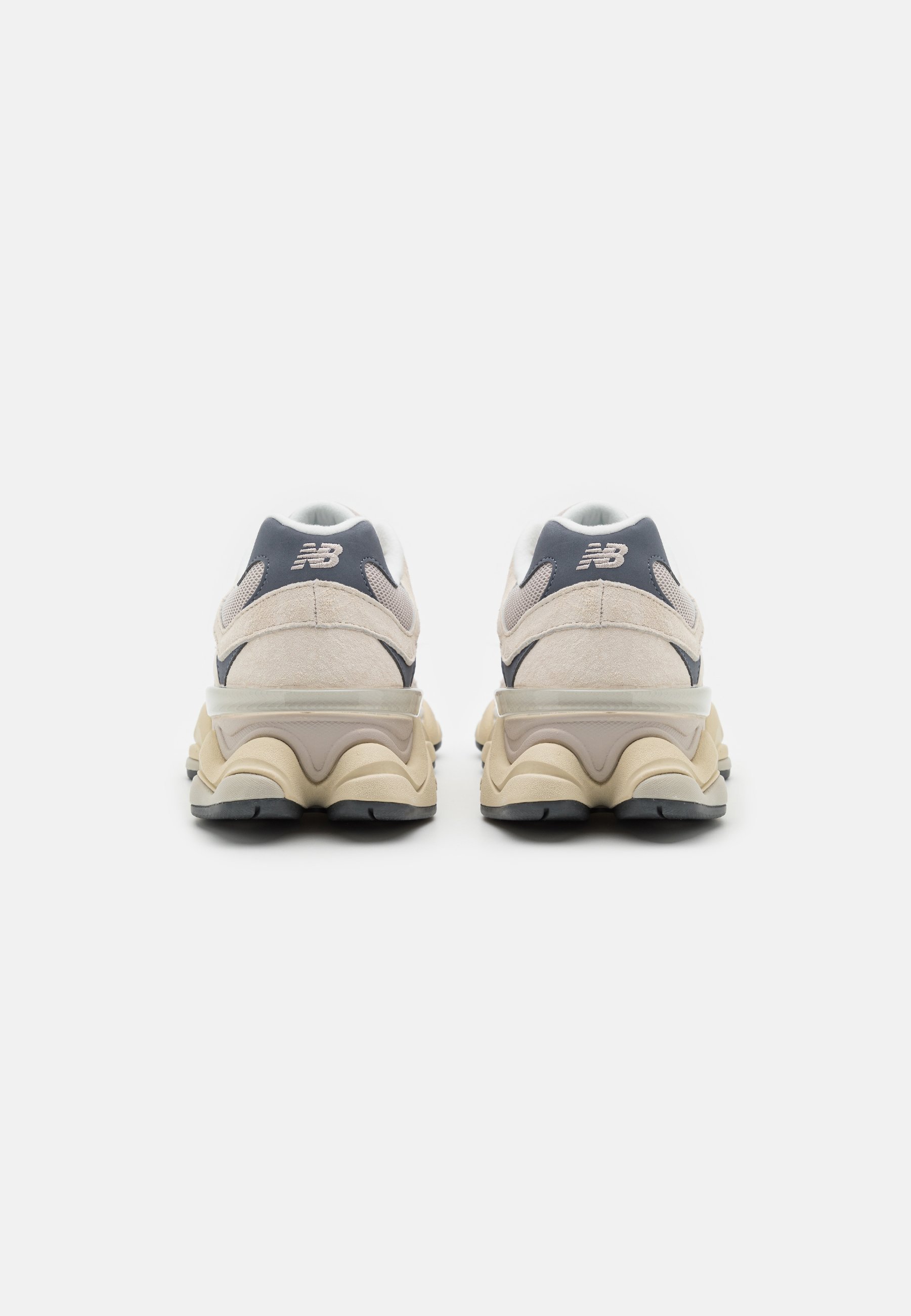 Zapatillas de deporte color beige claro con parte superior de ante y malla, con un acento en gris oscuro, suela acolchada y diseño de tacón elevado.