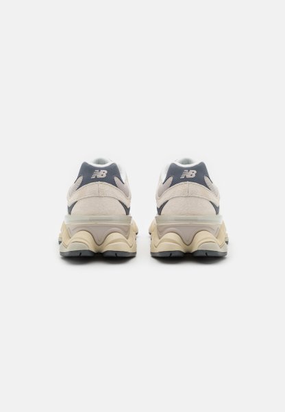 Zapatillas de deporte color beige claro con parte superior de ante y malla, con un acento en gris oscuro, suela acolchada y diseño de tacón elevado.