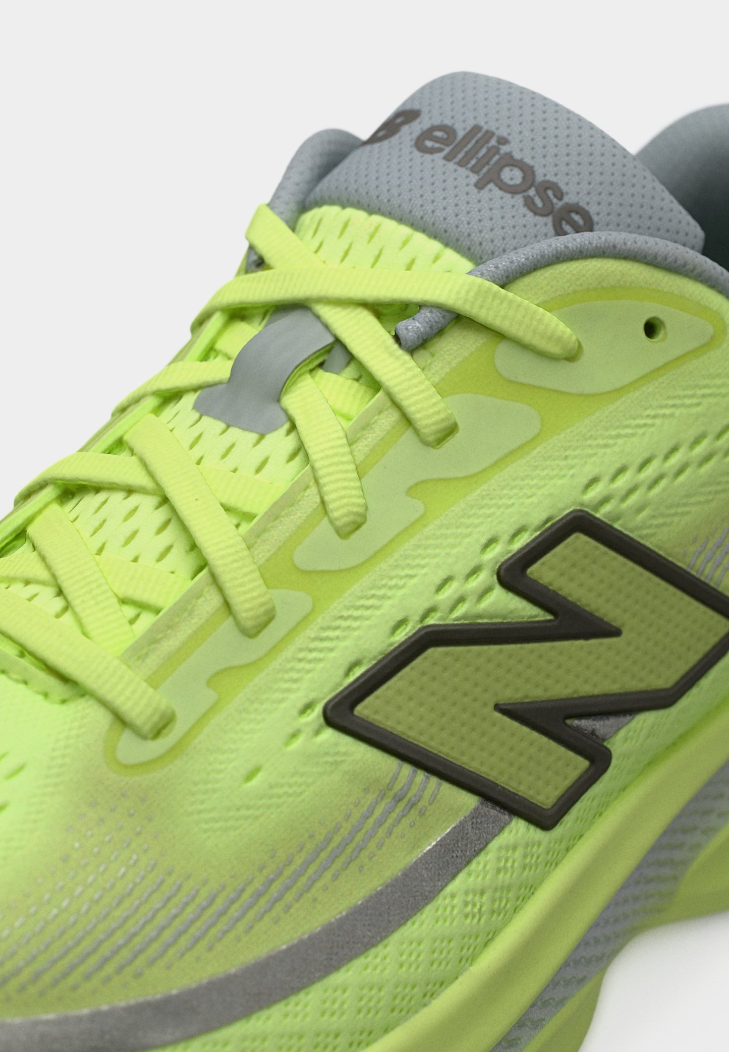 Primer plano de un zapato deportivo verde neón con lengüeta gris, cordones amarillos y un logo "N" verde oscuro en el lateral.
