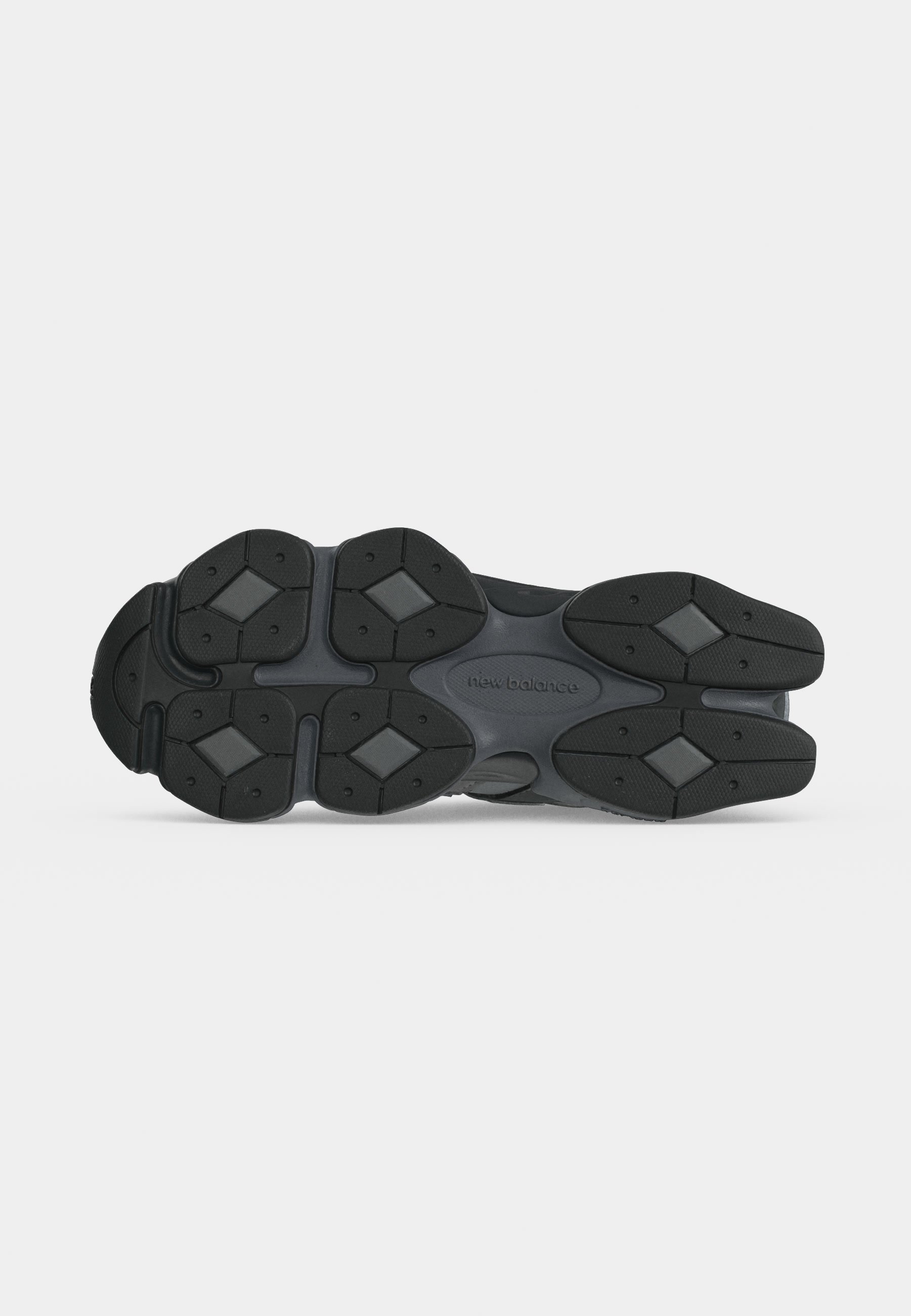 Suela de un zapato New Balance negro y gris oscuro con patrones de banda de rodadura en forma de diamante y agarres de goma texturizados.