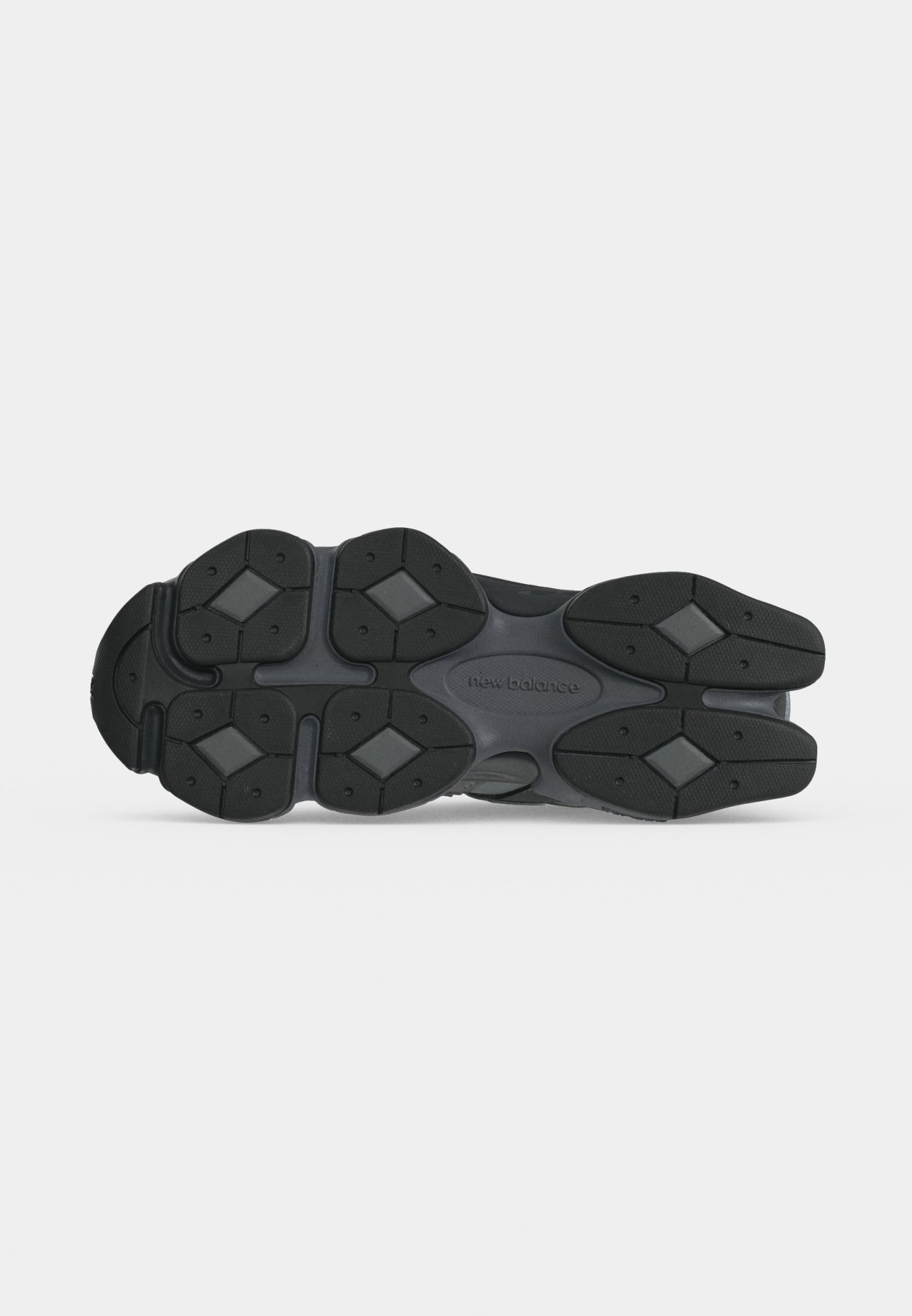 Suela de un zapato New Balance negro y gris oscuro con patrones de banda de rodadura en forma de diamante y agarres de goma texturizados.