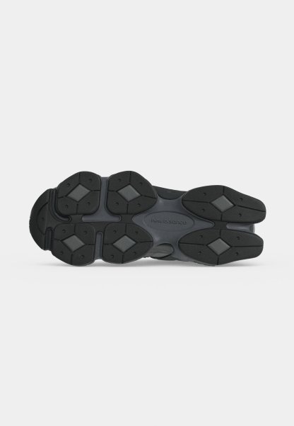 Suela de un zapato New Balance negro y gris oscuro con patrones de banda de rodadura en forma de diamante y agarres de goma texturizados.