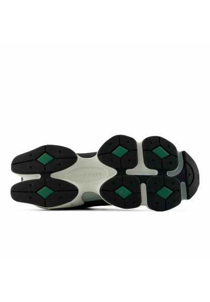 Suela de zapatilla New Balance en blanco y negro con detalles de agarre en forma de diamante verde y dibujo texturizado, vista desde abajo.