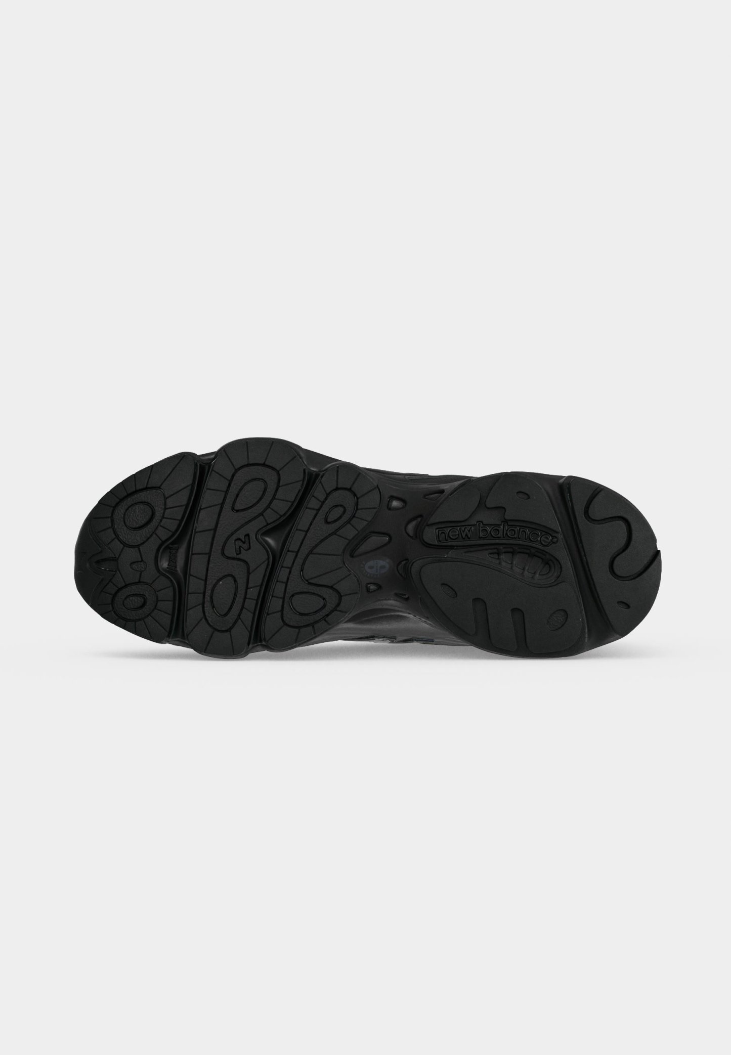 Suela negra de zapatilla New Balance con patrones texturizados antideslizantes y logo en relieve cerca del talón sobre un fondo gris claro liso.