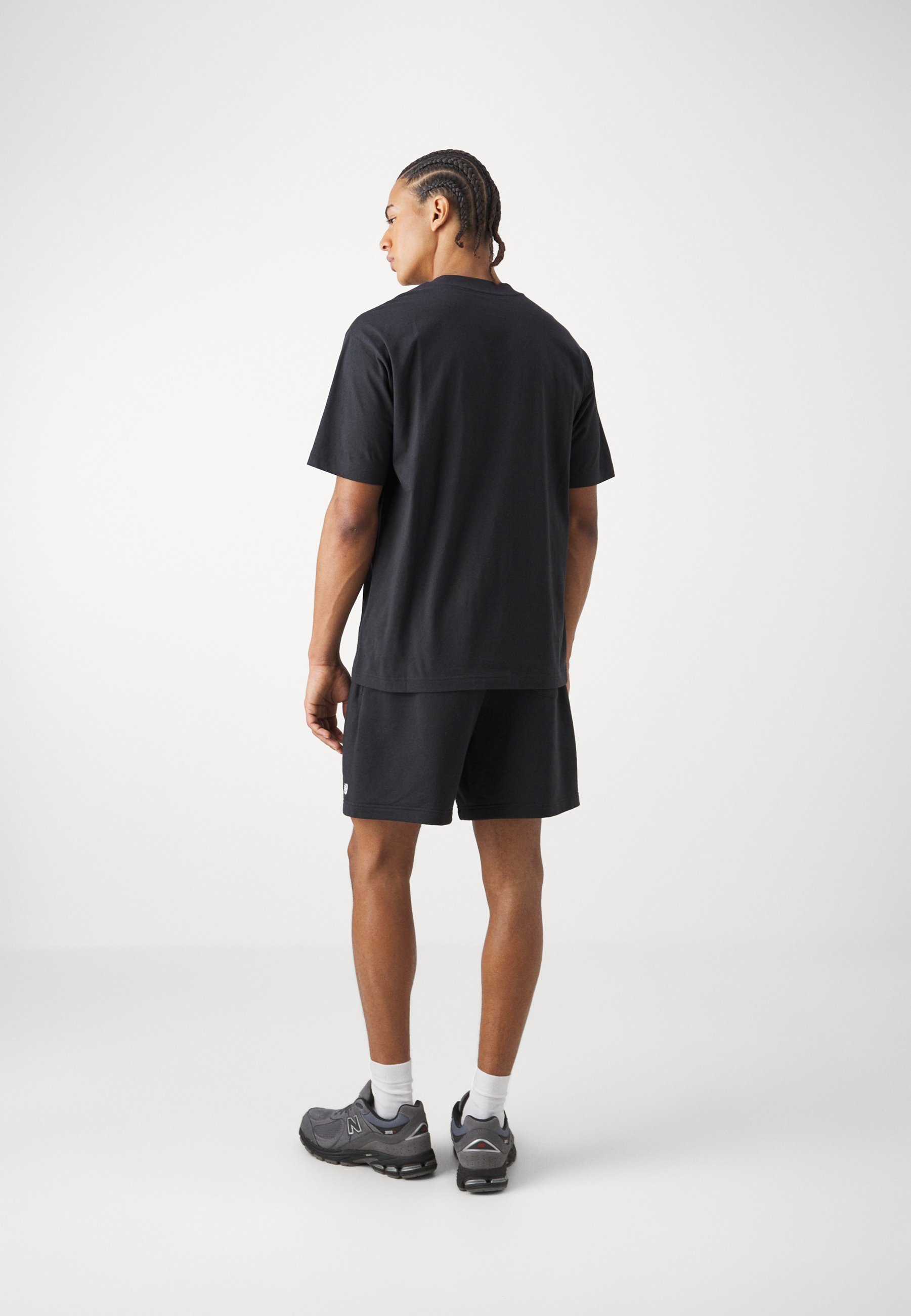 Conjunto de camiseta negra de manga corta y pantalones cortos, hecho de algodón, con un corte relajado y combinado con zapatillas deportivas grises y calcetines blancos.