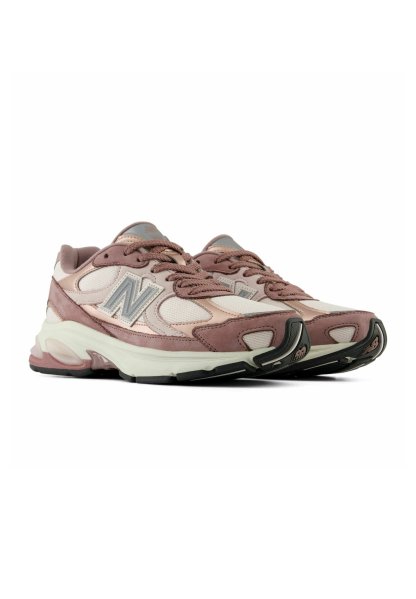 Par de zapatillas deportivas New Balance rosa y blancas con parte superior de malla y ante y suelas blancas gruesas, vistas desde un ángulo frontal lateral.