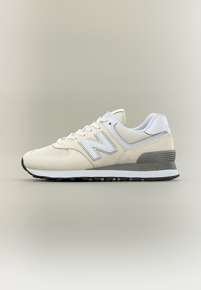 Zapatilla New Balance beige y blanca con entresuela gris y suela exterior negra, con materiales de malla y ante y diseño con cordones.
