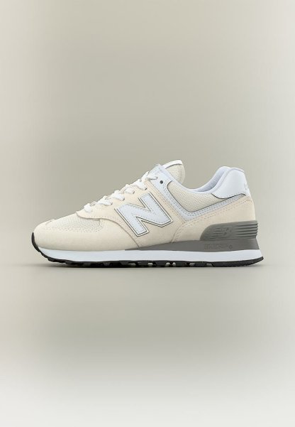 Zapatilla New Balance beige y blanca con entresuela gris y suela exterior negra, con materiales de malla y ante y diseño con cordones.