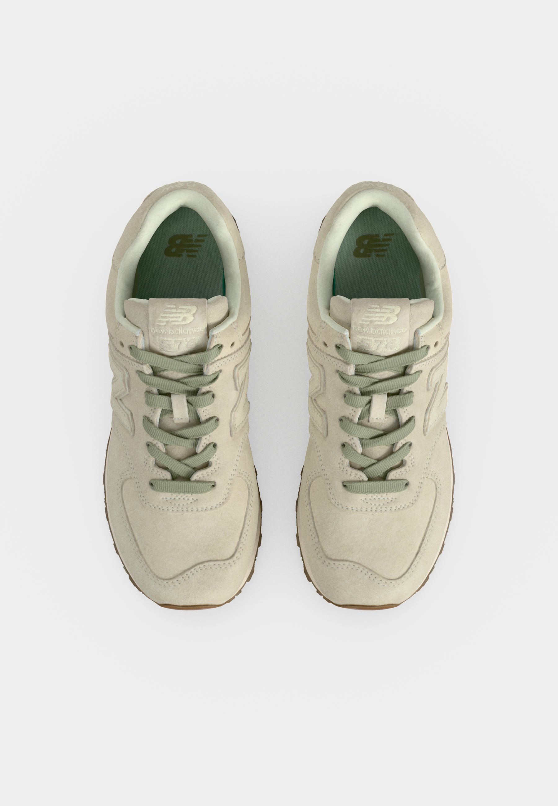 Par de zapatillas New Balance beige con cordones verdes y forro interior, mostradas desde arriba sobre un fondo blanco.