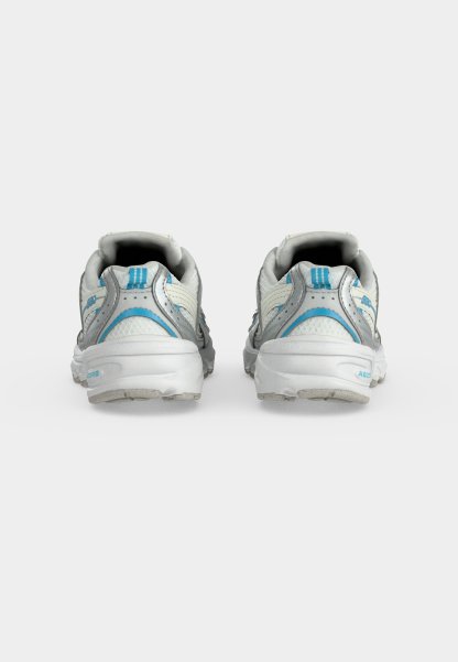 Par de zapatillas deportivas blancas y azul claro vistas desde atrás sobre un fondo gris claro liso.