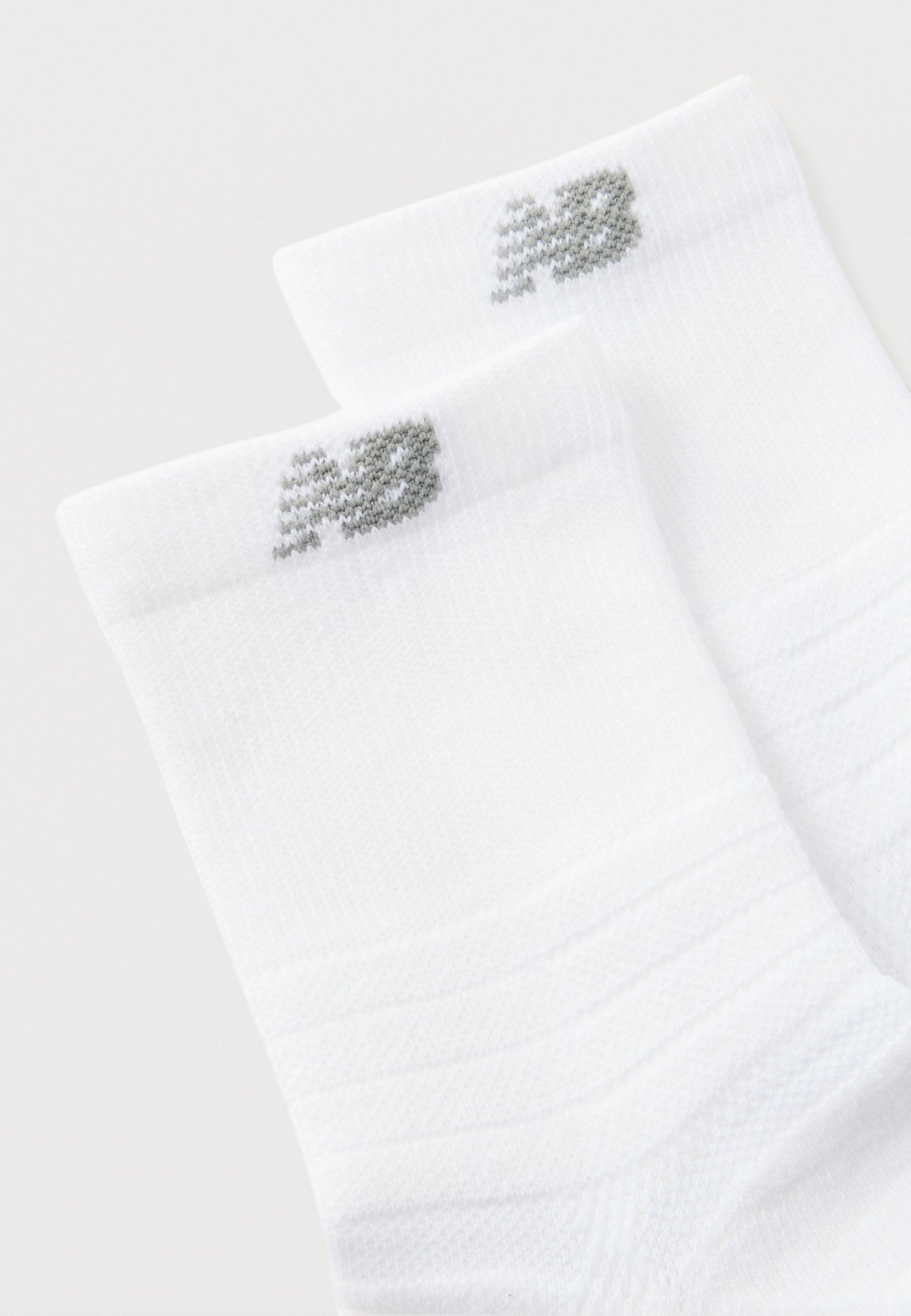 Calcetines tobilleros blancos con textura acanalada y logo "NB" gris cerca del borde superior, mostrados sobre un fondo liso.