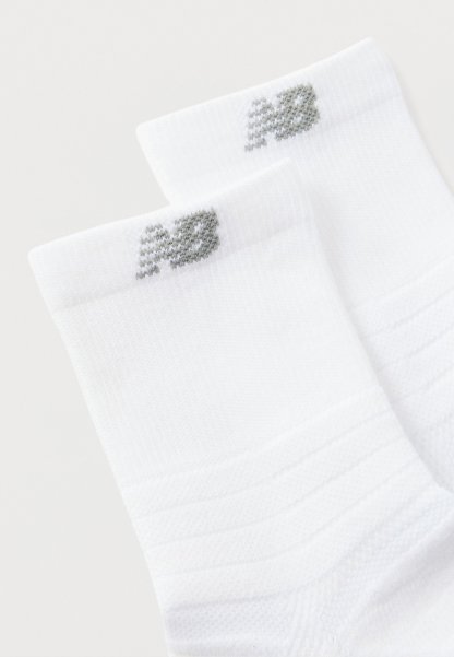 Calcetines tobilleros blancos con textura acanalada y logo "NB" gris cerca del borde superior, mostrados sobre un fondo liso.