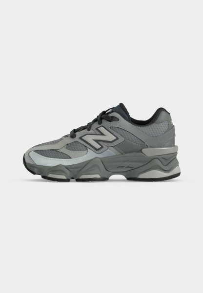 Zapatilla deportiva gris y negra con paneles de malla y cuero, cordones negros, suela acolchada y logo "N" en el lateral.