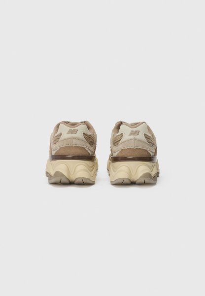 Zapatillas marrones y beige con un upper de ante texturizado, paneles de malla y una suela con patrón de olas. Presentan un logo reflectante en el talón.