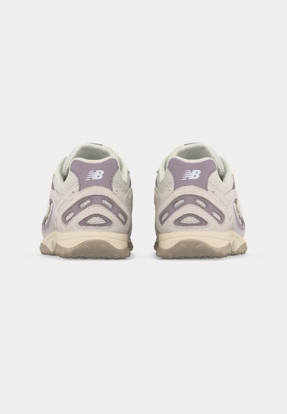 Par de zapatillas New Balance beige y moradas mostradas desde atrás sobre un fondo gris liso.
