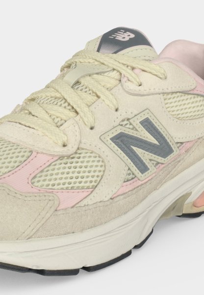 Zapatilla New Balance beige y rosa con detalles de malla y ante, cordones crema y un logo gris "N" en el lateral.