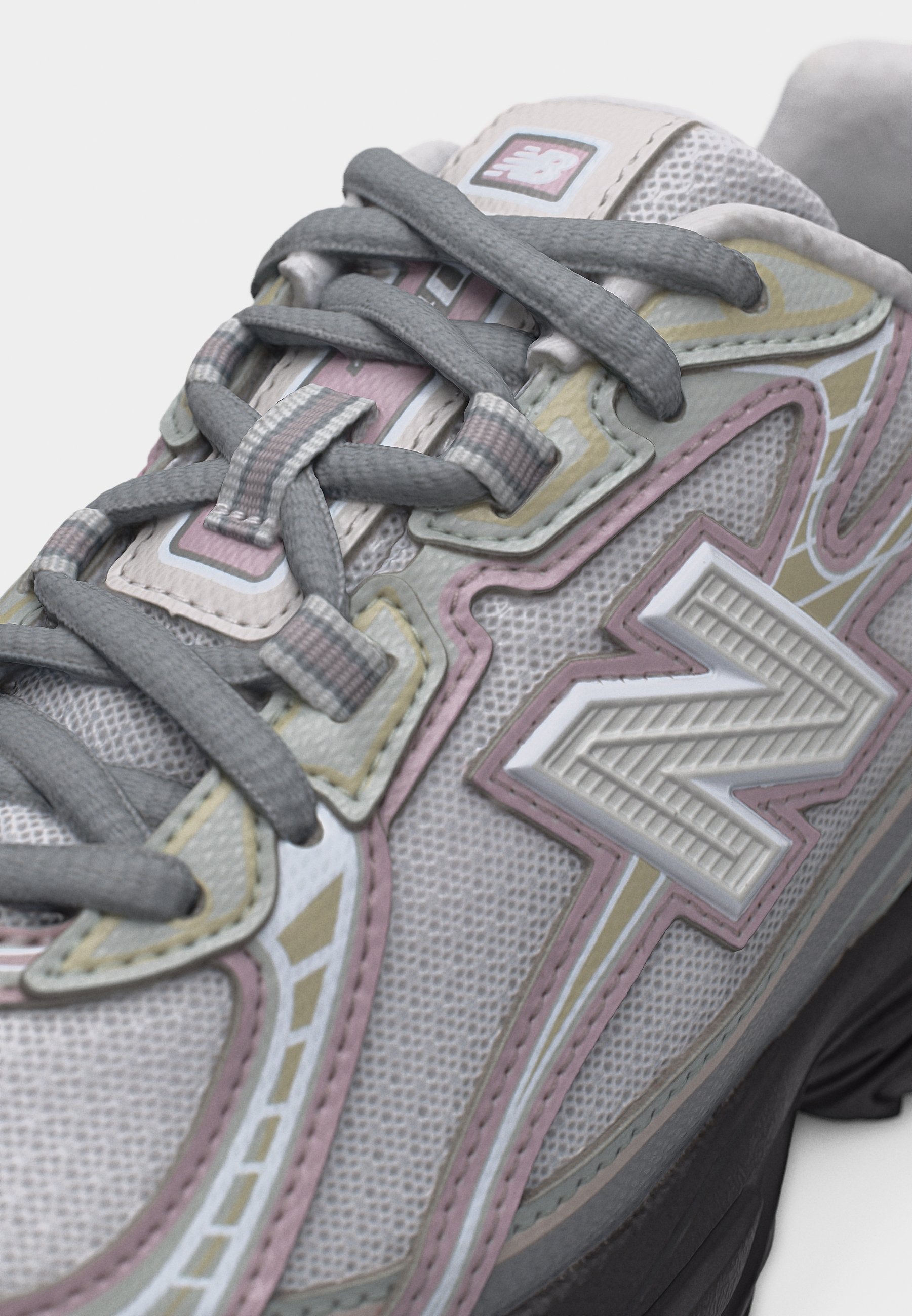 Primer plano de una zapatilla New Balance gris y rosa pastel con tela de malla texturizada y cordones grises gruesos atados cuidadosamente.