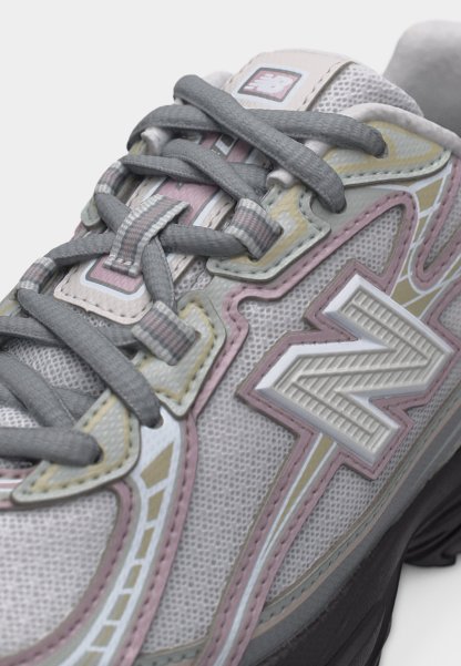 Primer plano de una zapatilla New Balance gris y rosa pastel con tela de malla texturizada y cordones grises gruesos atados cuidadosamente.