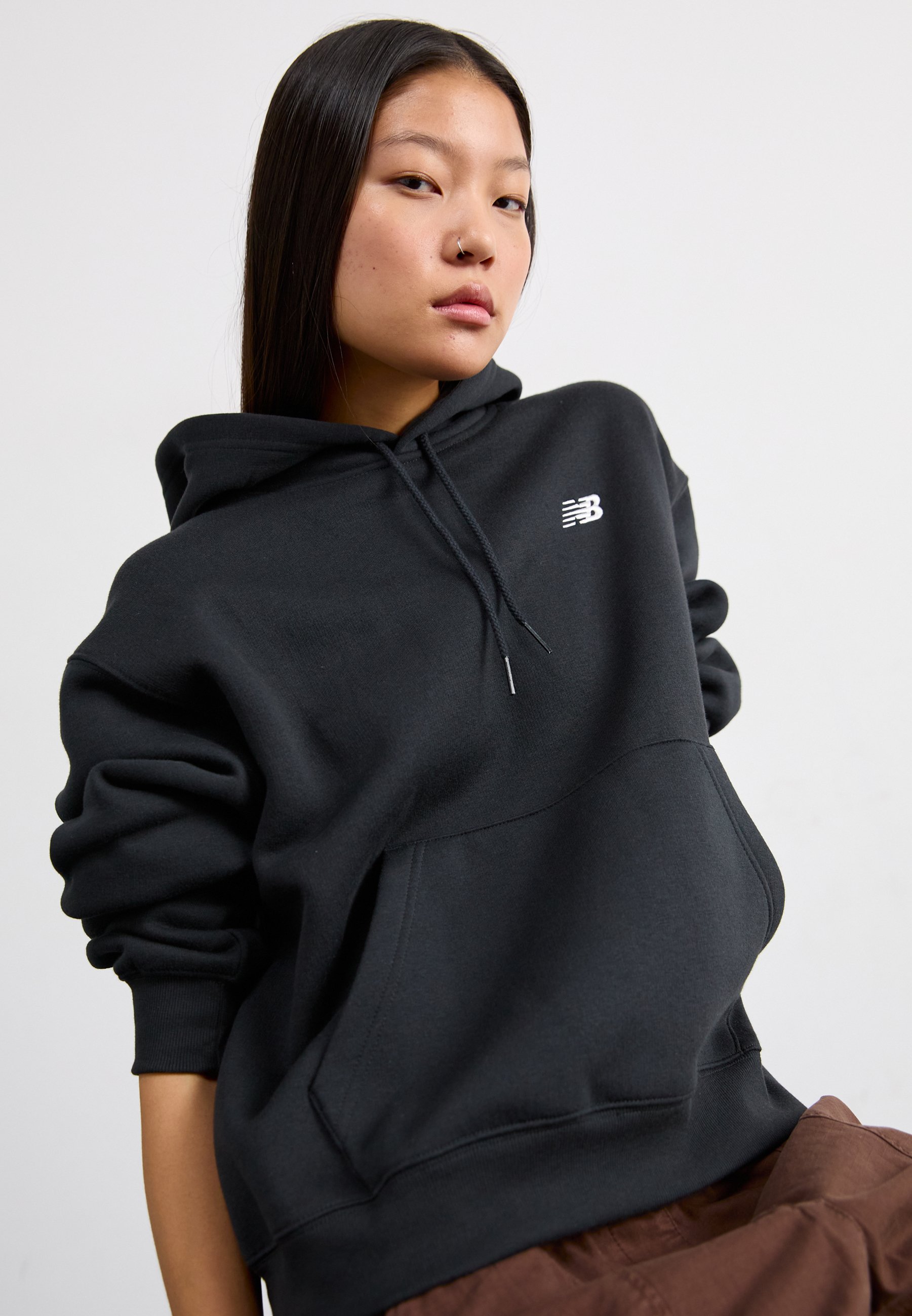 Sudadera negra con capucha ajustable, gran bolsillo frontal, puños acanalados y un logo blanco en el pecho. Tejido suave y grueso con una textura lisa.