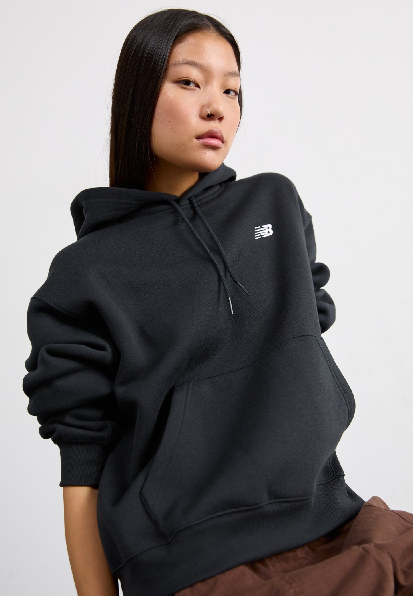 Sudadera negra con capucha ajustable, gran bolsillo frontal, puños acanalados y un logo blanco en el pecho. Tejido suave y grueso con una textura lisa.