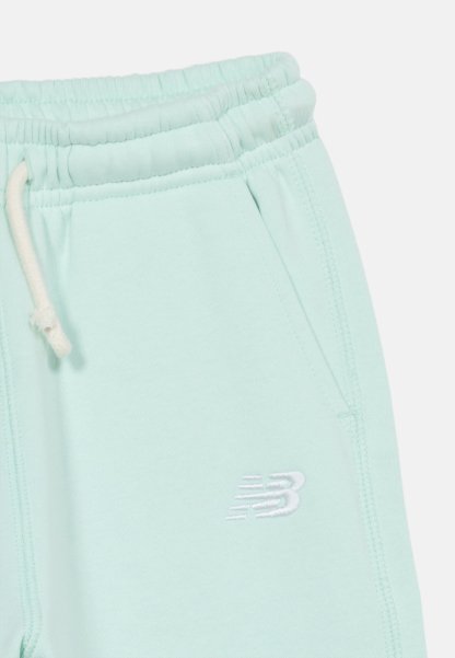 Pantalones deportivos azul claro con cintura elástica, cordón blanco, bolsillos laterales y pequeño logo blanco de New Balance en la pierna derecha.
