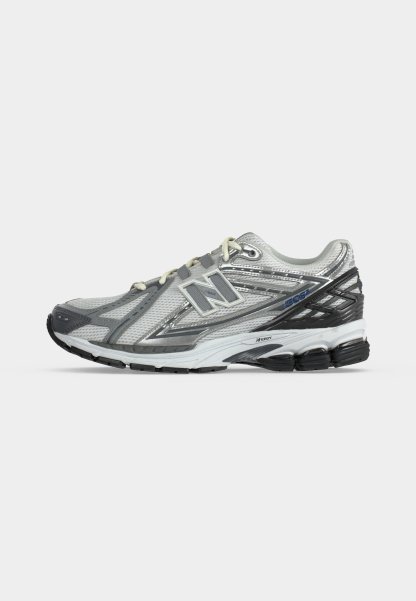 Zapatilla de correr New Balance blanca y gris con parte superior de malla, suela acolchada y suela exterior de goma negra, mostrada de perfil sobre fondo neutro.
