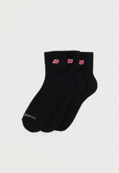 Tres pares de calcetines negros hasta el tobillo con logotipos de New Balance en rojo y blanco en los puños y una marca sutil en las puntas.