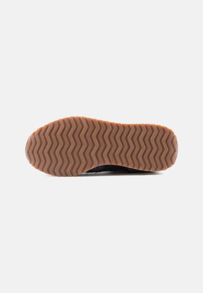 Suela de zapato con banda de rodadura de goma marrón que presenta un patrón en zigzag y pequeño texto de la marca en cada cresta, mostrado sobre un fondo blanco.