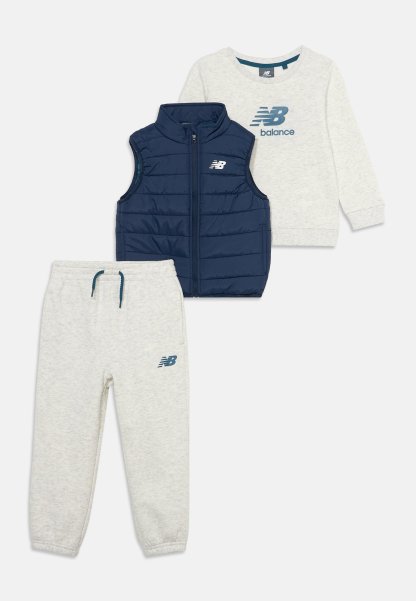 Conjunto de ropa infantil con sudadera gris claro de manga larga, pantalones deportivos a juego y chaleco acolchado sin mangas azul marino, todos con logos de New Balance.