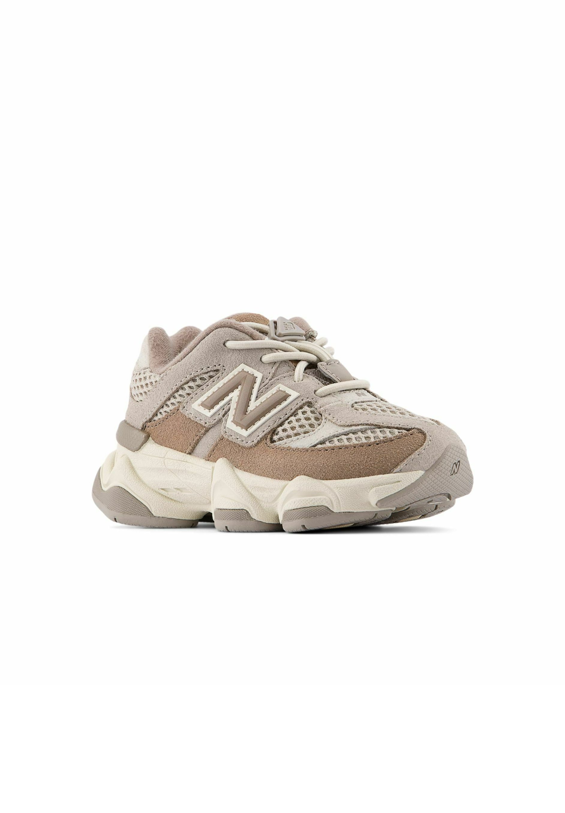 Zapatilla New Balance beige y topo con paneles de malla y ante, suela gruesa, cordones delanteros y logo "N" en el lateral.