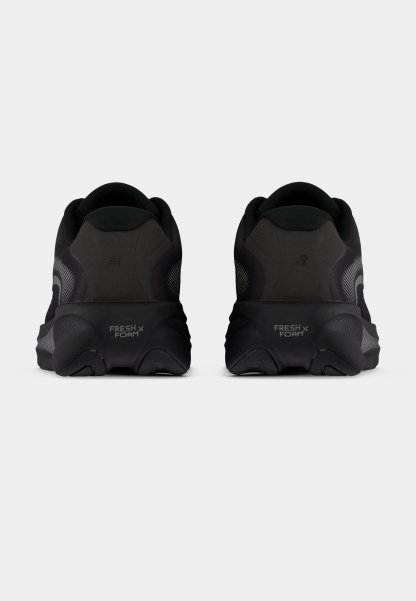 Zapatillas de running negras con parte superior de malla texturizada, suela acolchada y la marca "FRESH FOAM" en el talón. Diseño redondeado y estilo minimalista.