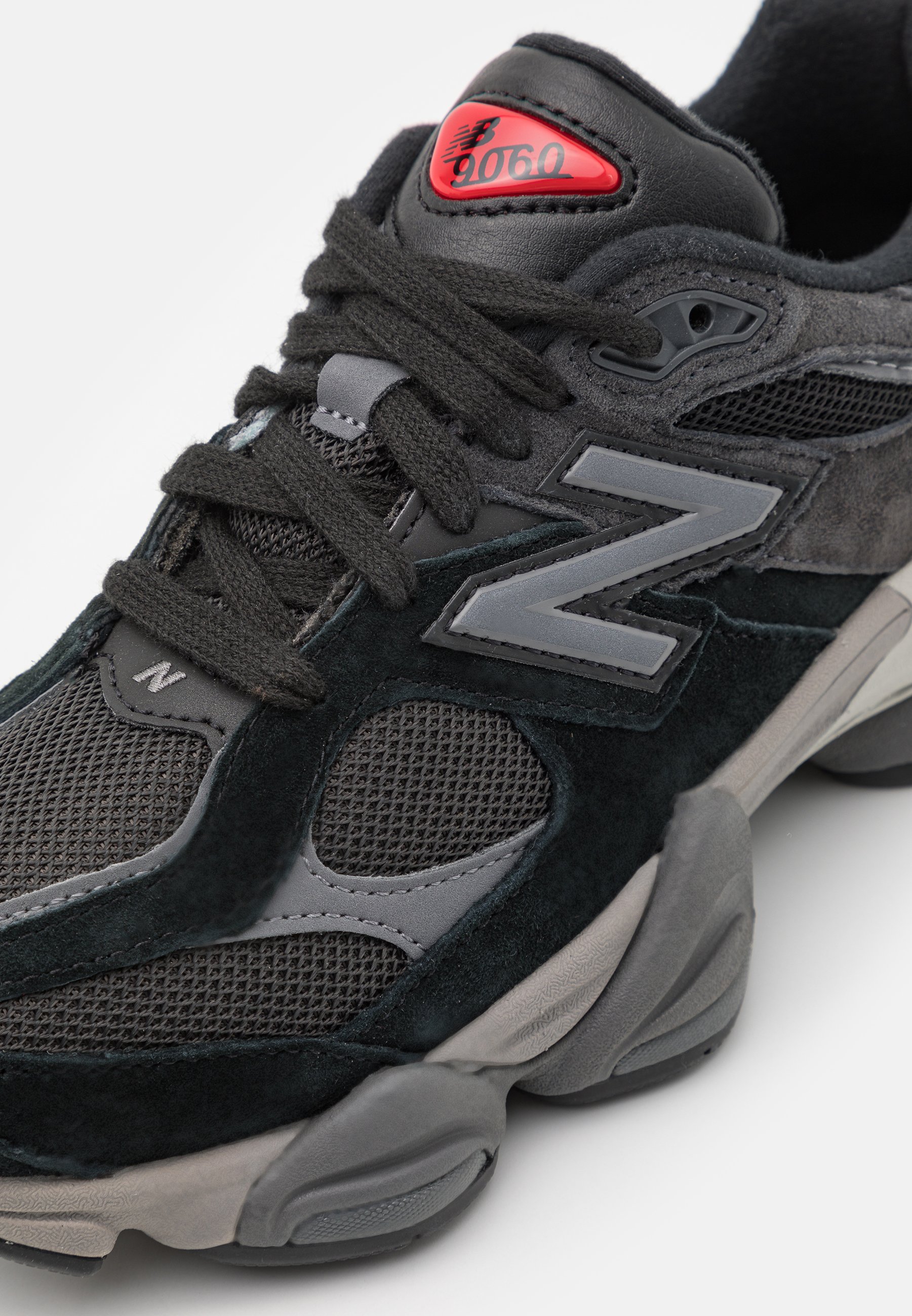 Zapatilla negra y gris con upper de malla y ante, con un destacado logo gris de "N", etiqueta roja y suela texturizada para tracción.