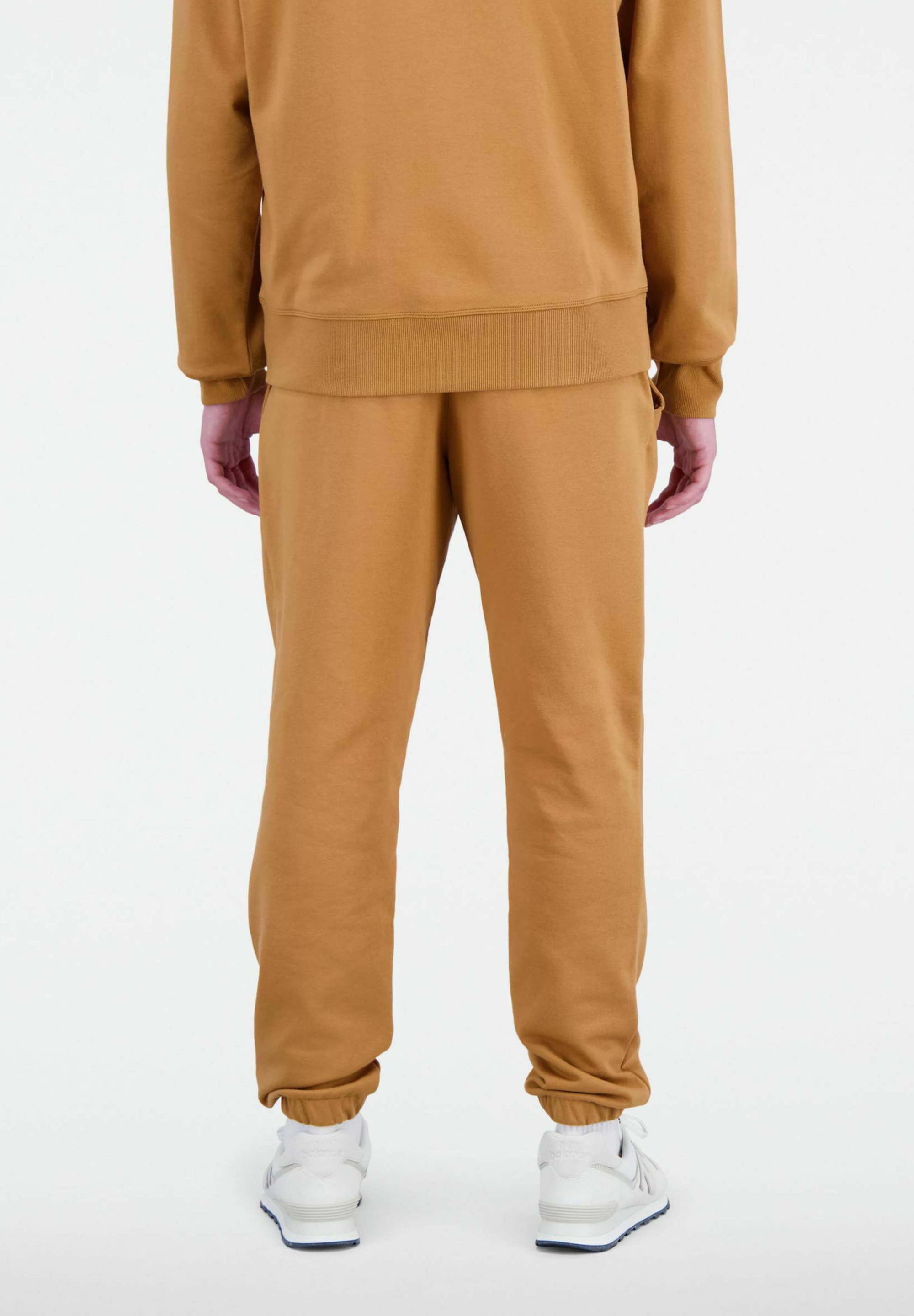 Pantalones de chándal de algodón beige con cintura y puños elásticos. Combinados con zapatillas blancas. La tela parece suave y lisa.