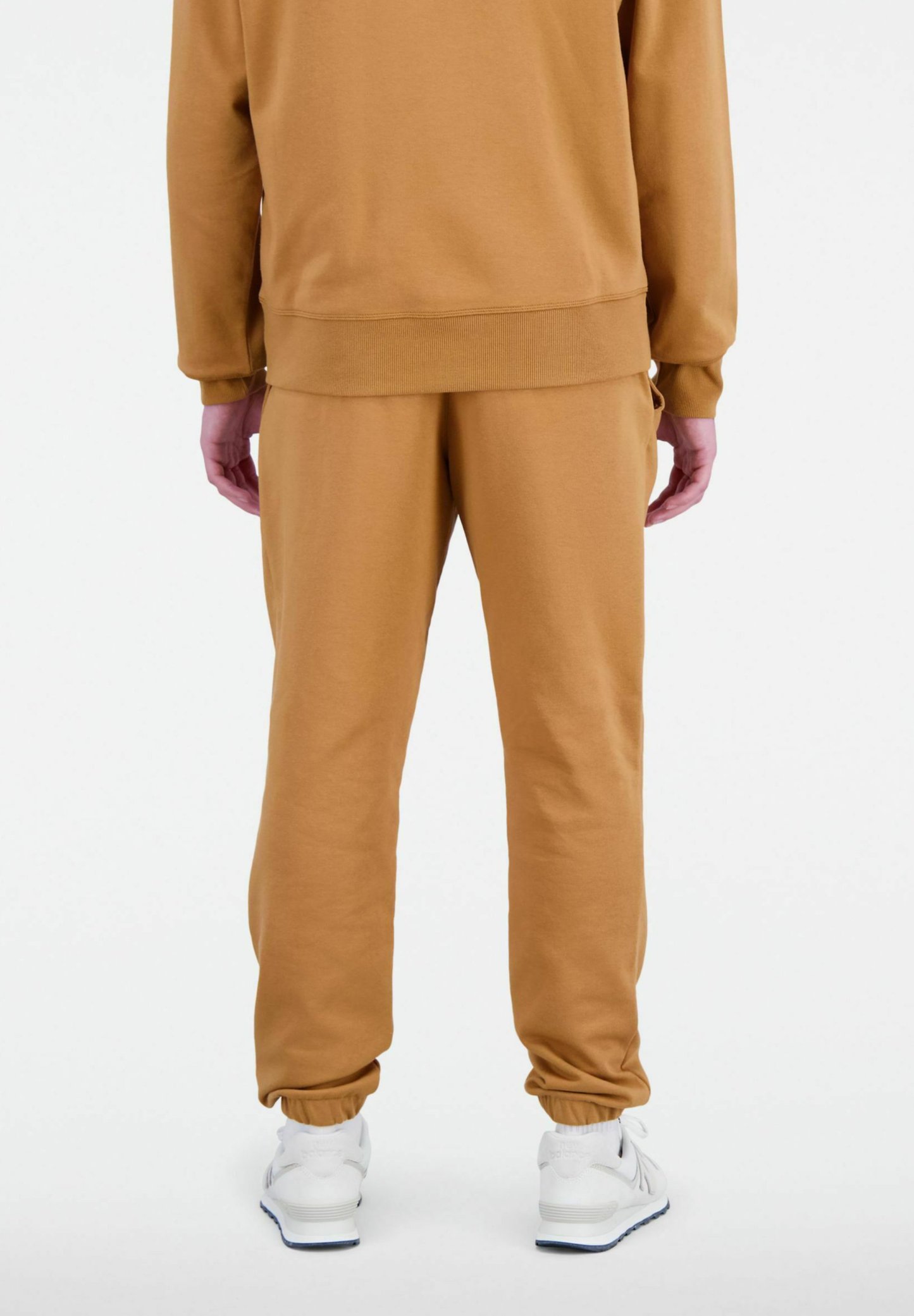 Pantalones de chándal de algodón beige con cintura y puños elásticos. Combinados con zapatillas blancas. La tela parece suave y lisa.