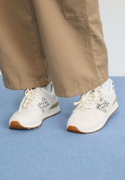 Zapatillas blancas con detalles de estampado de leopardo, usadas con pantalones anchos beige sobre una alfombra azul claro.
