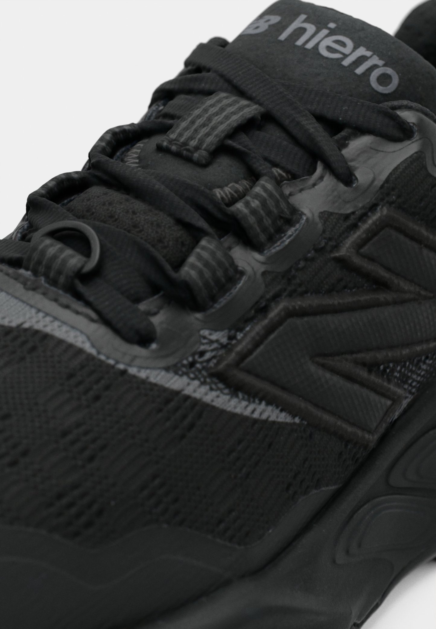 Zapatilla deportiva negra con parte superior texturizada, acentos lisos y un sistema de cordones pronunciado. Logotipo ubicado en la lengüeta, diseño elegante.