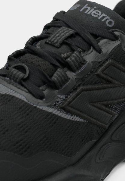 Zapatilla deportiva negra con parte superior texturizada, acentos lisos y un sistema de cordones pronunciado. Logotipo ubicado en la lengüeta, diseño elegante.