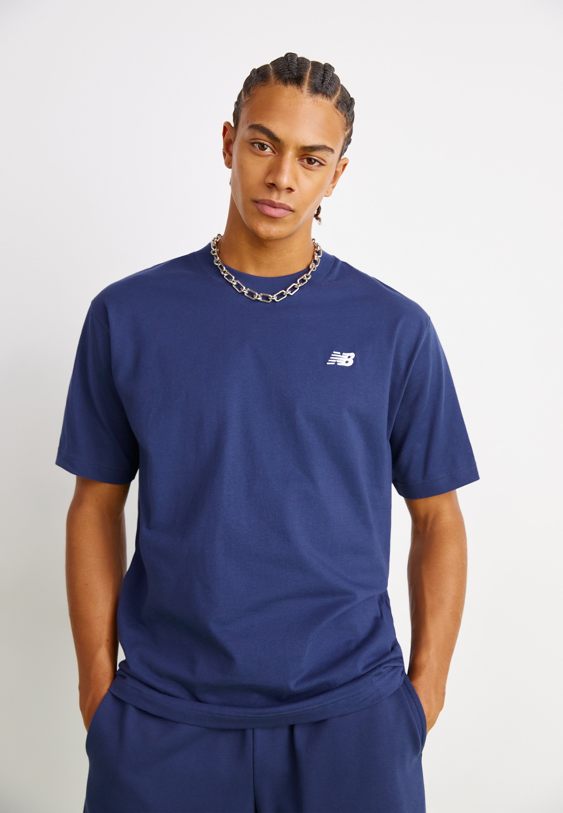 Camiseta de algodón azul marino con mangas cortas, escote redondo y un pequeño logotipo blanco de New Balance en el lado izquierdo del pecho. Textura suave.