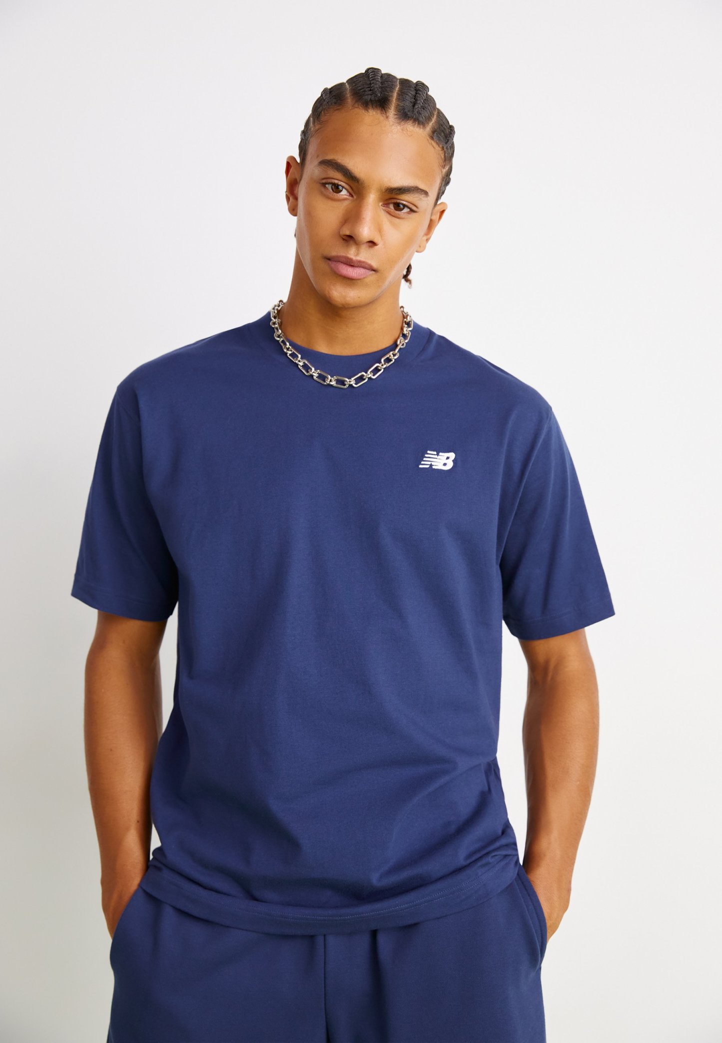 Camiseta de algodón azul marino con mangas cortas, escote redondo y un pequeño logotipo blanco de New Balance en el lado izquierdo del pecho. Textura suave.