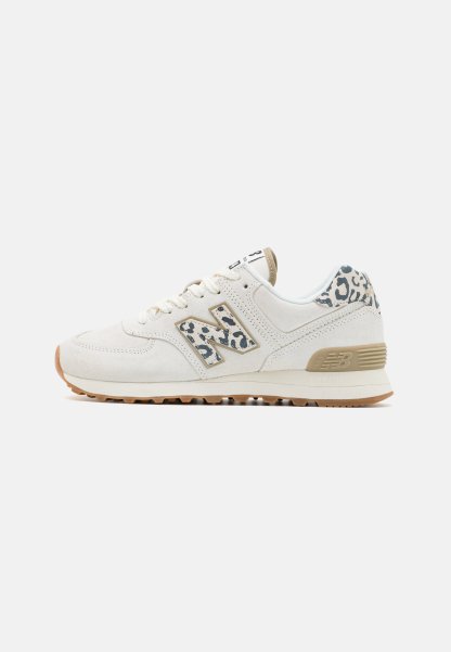 Zapatilla blanca New Balance con suela beige y detalles de estampado de leopardo en el talón y el logo, cierre de cordones, vista de perfil lateral.