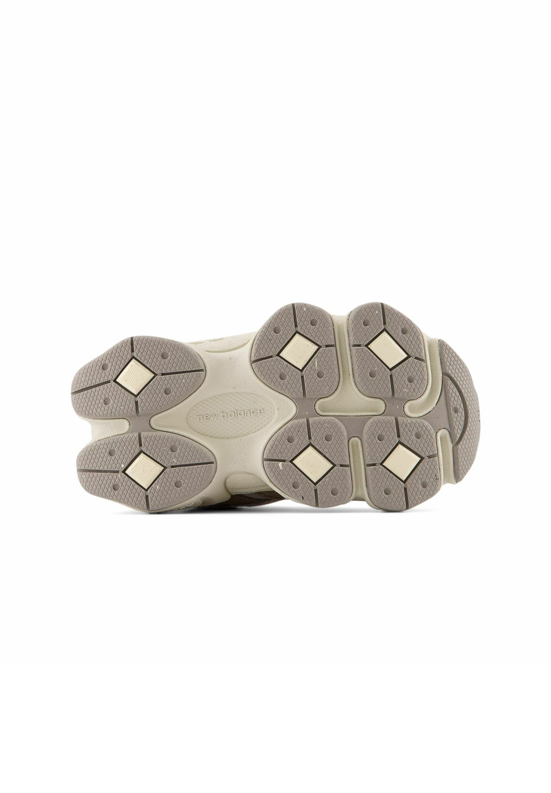 Suela de zapato con secciones de goma beige y gris, patrones de diamantes y áreas de agarre texturizadas, mostrando la marca New Balance en el centro.