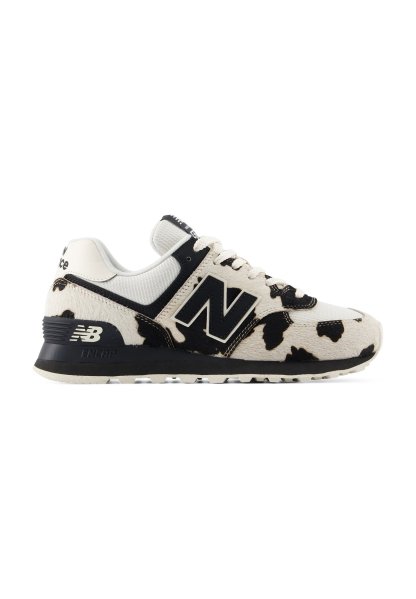 Zapatilla New Balance blanca y negra con estampado de vaca, suela negra y detalles de tela de malla, vista desde el lateral.