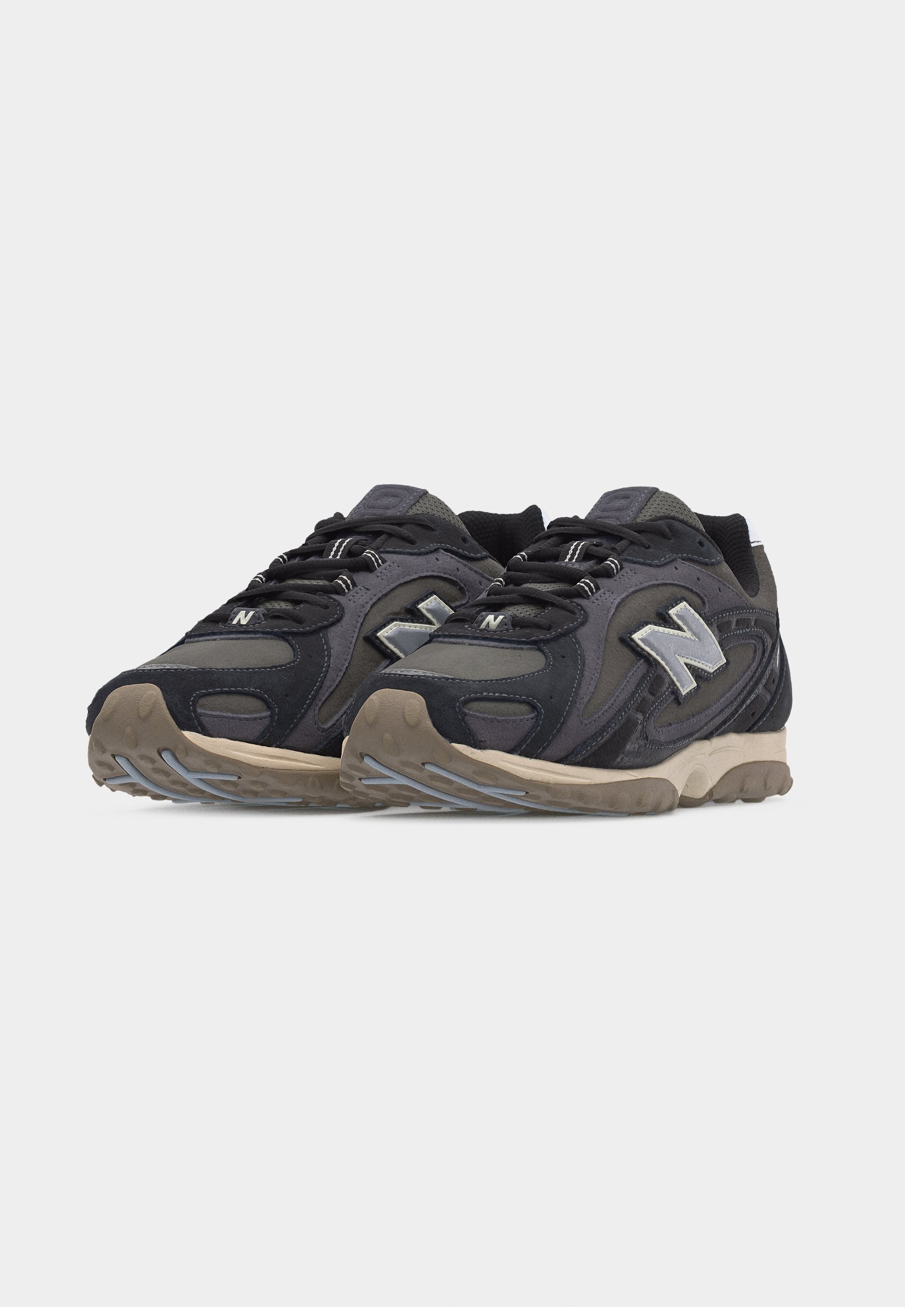 Par de zapatillas New Balance negras y grises con suelas beige, diseño con cordones y destacado logo "N" en los laterales.