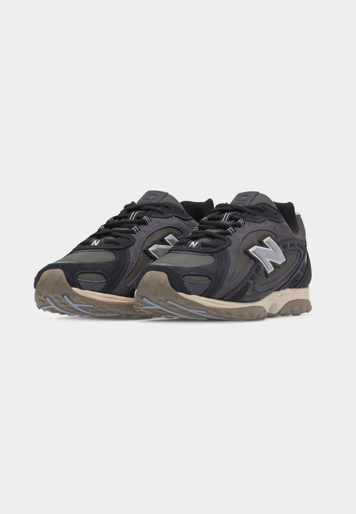 Par de zapatillas New Balance negras y grises con suelas beige, diseño con cordones y destacado logo "N" en los laterales.