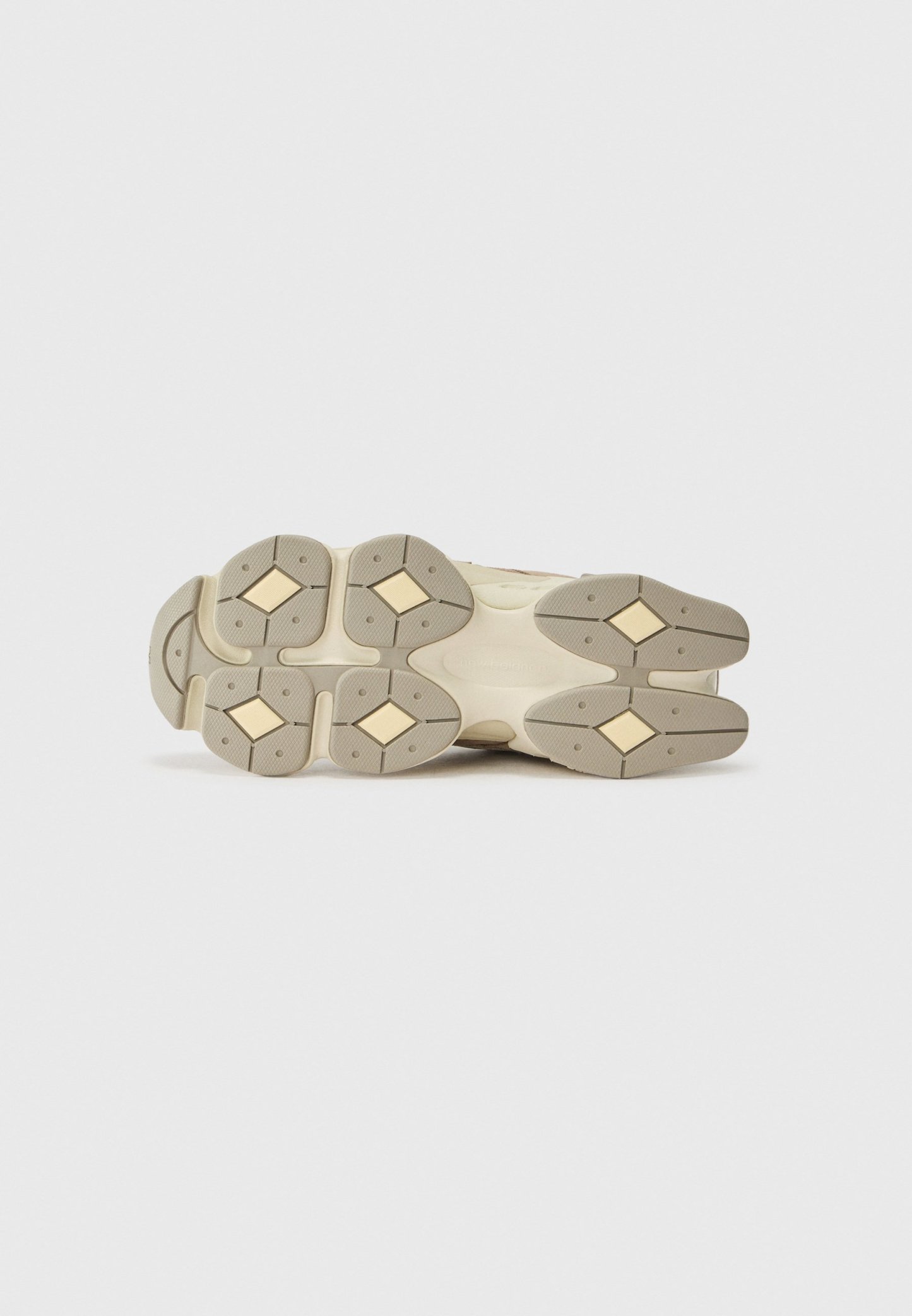 Suela de zapato que presenta un goma beige duradera con un patrón de diamante en relieve, acentos dorados y un dibujo distintivo para agarre y tracción.