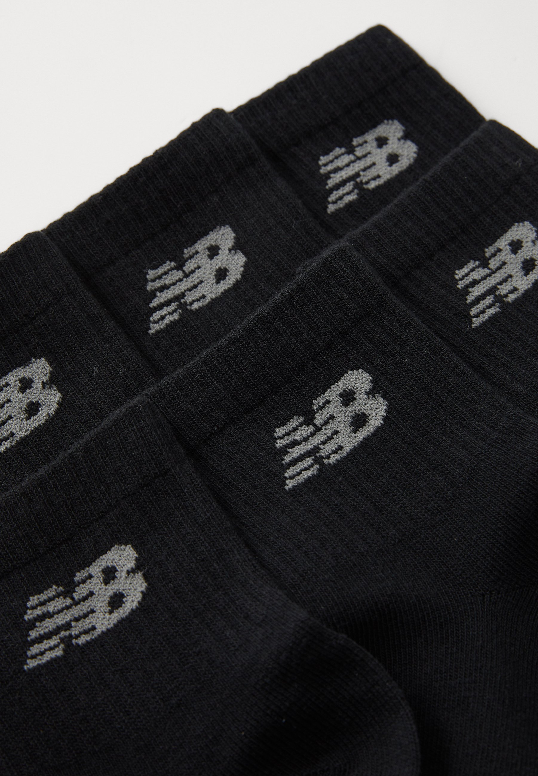 Calcetines negros con textura acanalada, que presentan un logo gris de New Balance en el puño. Diseño simple sin patrones o acentos adicionales.