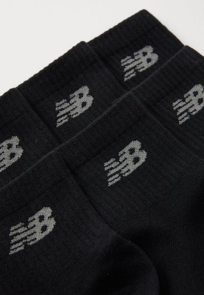Calcetines negros con textura acanalada, que presentan un logo gris de New Balance en el puño. Diseño simple sin patrones o acentos adicionales.