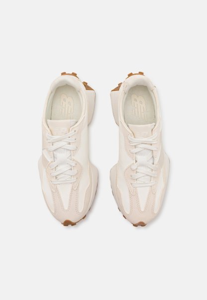 Zapatillas deportivas de color beige claro y blanco con parte superior texturizada, cierre de cordones y suela de goma. Presentan un diseño de panel único y detalles de costura.